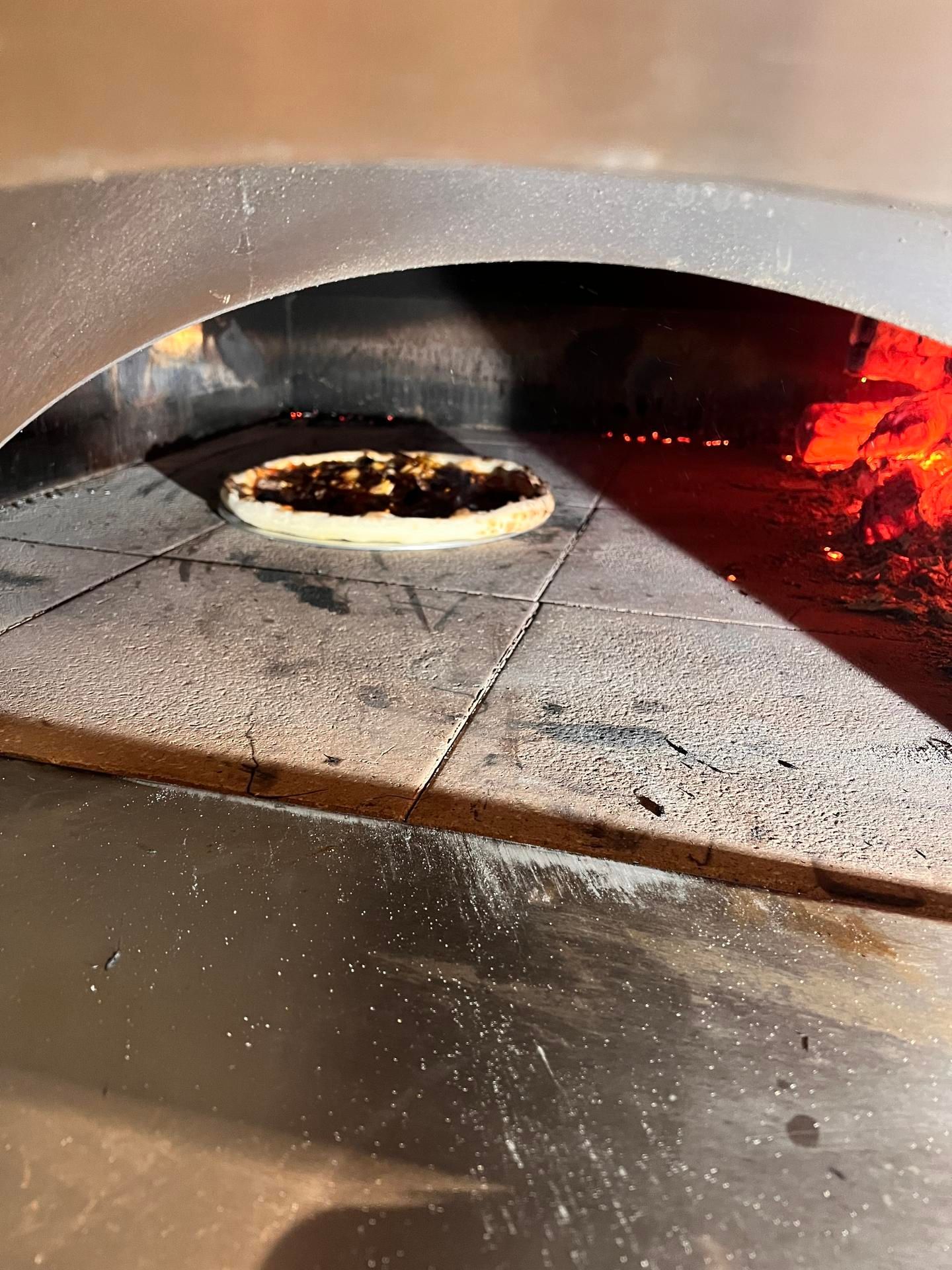 Pizza cuite dans un four à bois, avec des braises incandescentes et une sole en pierre.