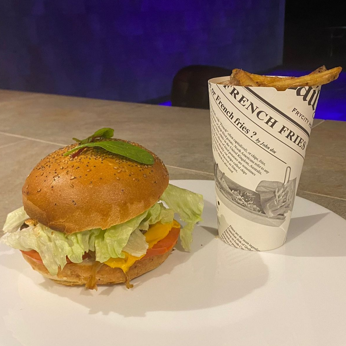 Un hamburger et des frites sur une table, dans un cornet en papier et son emballage.