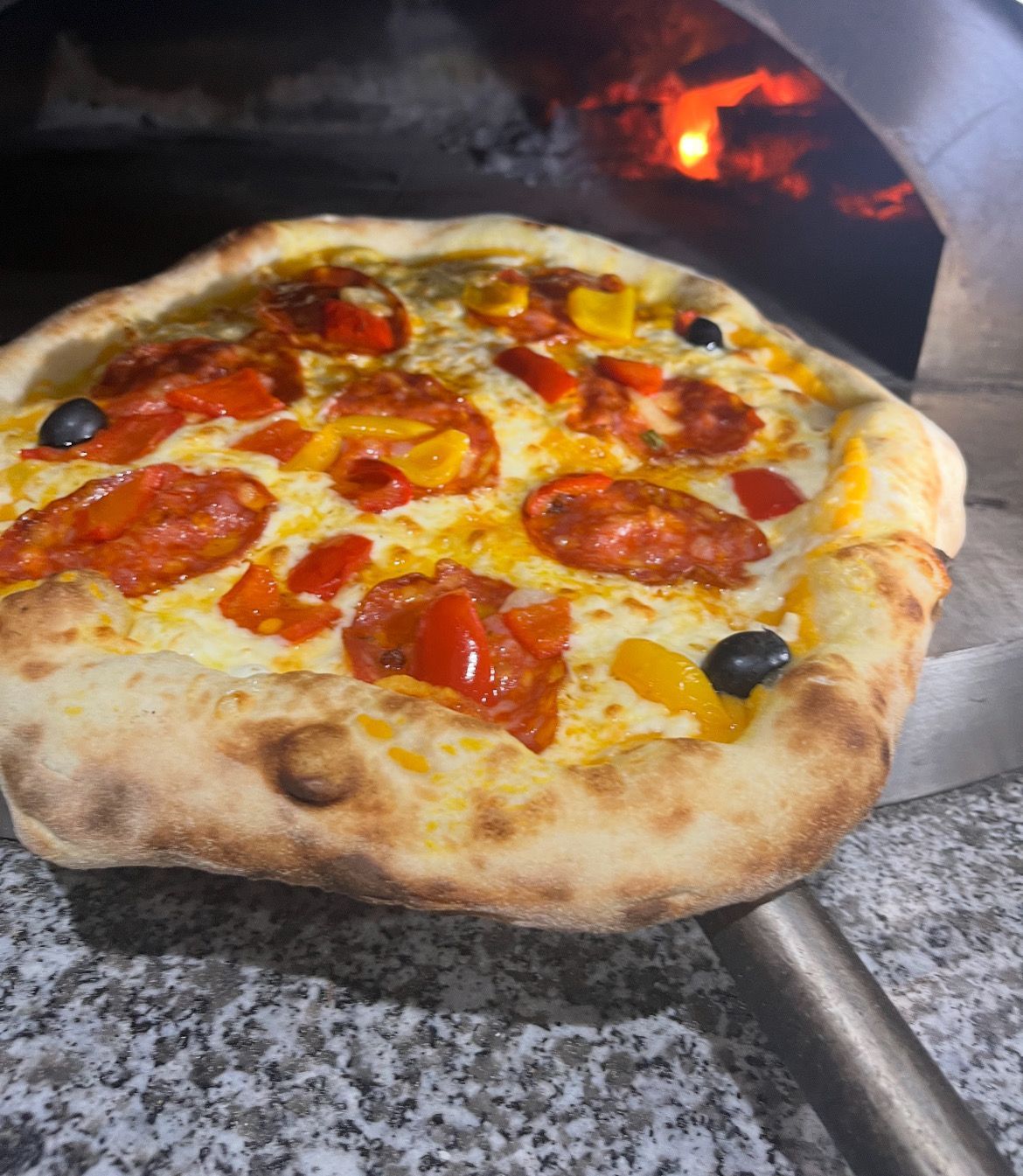 Une pizza fraîche au pepperoni, sur une pelle à pizza, avec du fromage fondu et des olives, sortie du four à bois.