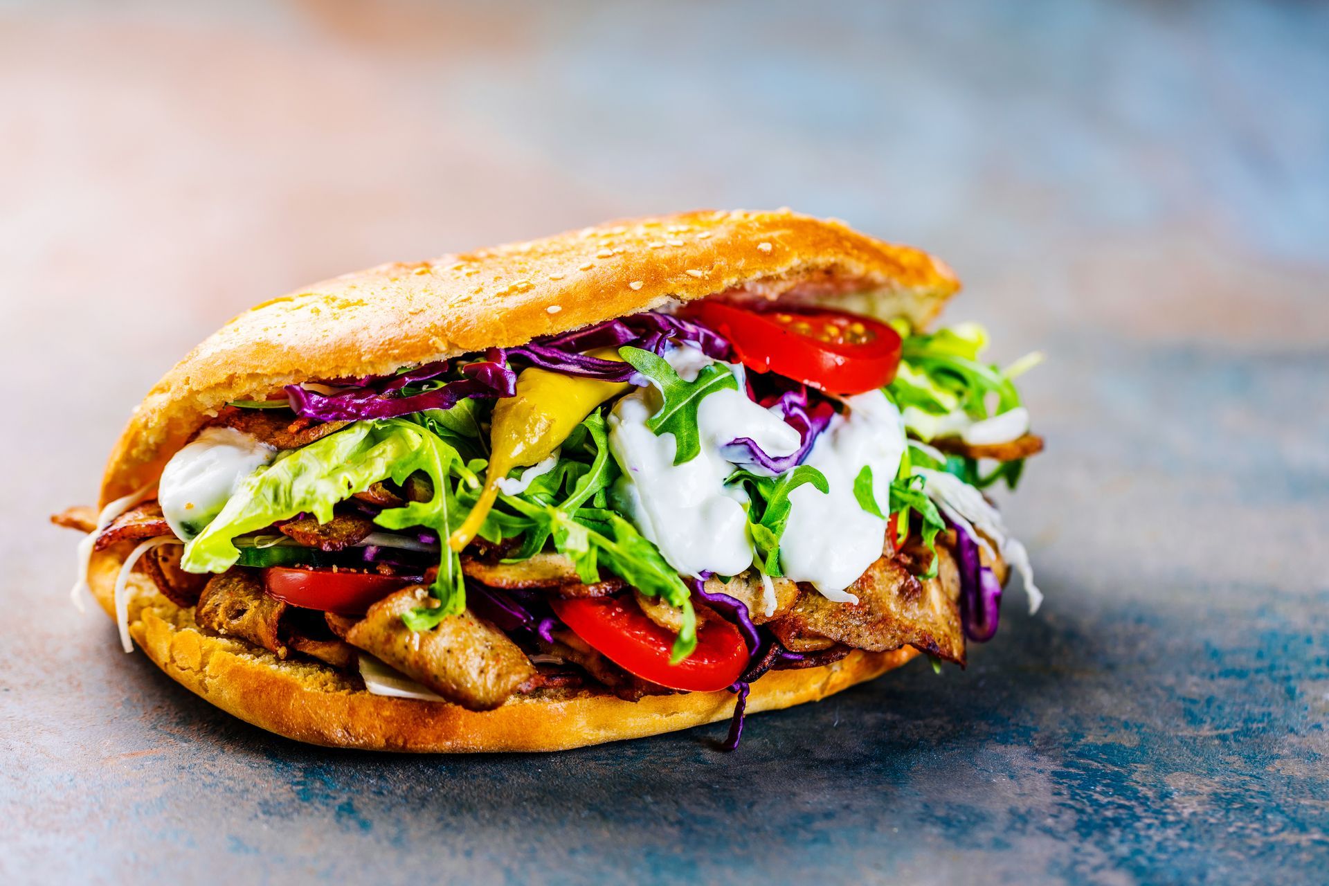 Sandwich grillé garni de légumes verts, de poivrons rouges et de sauce blanche, servi sur une surface rustique