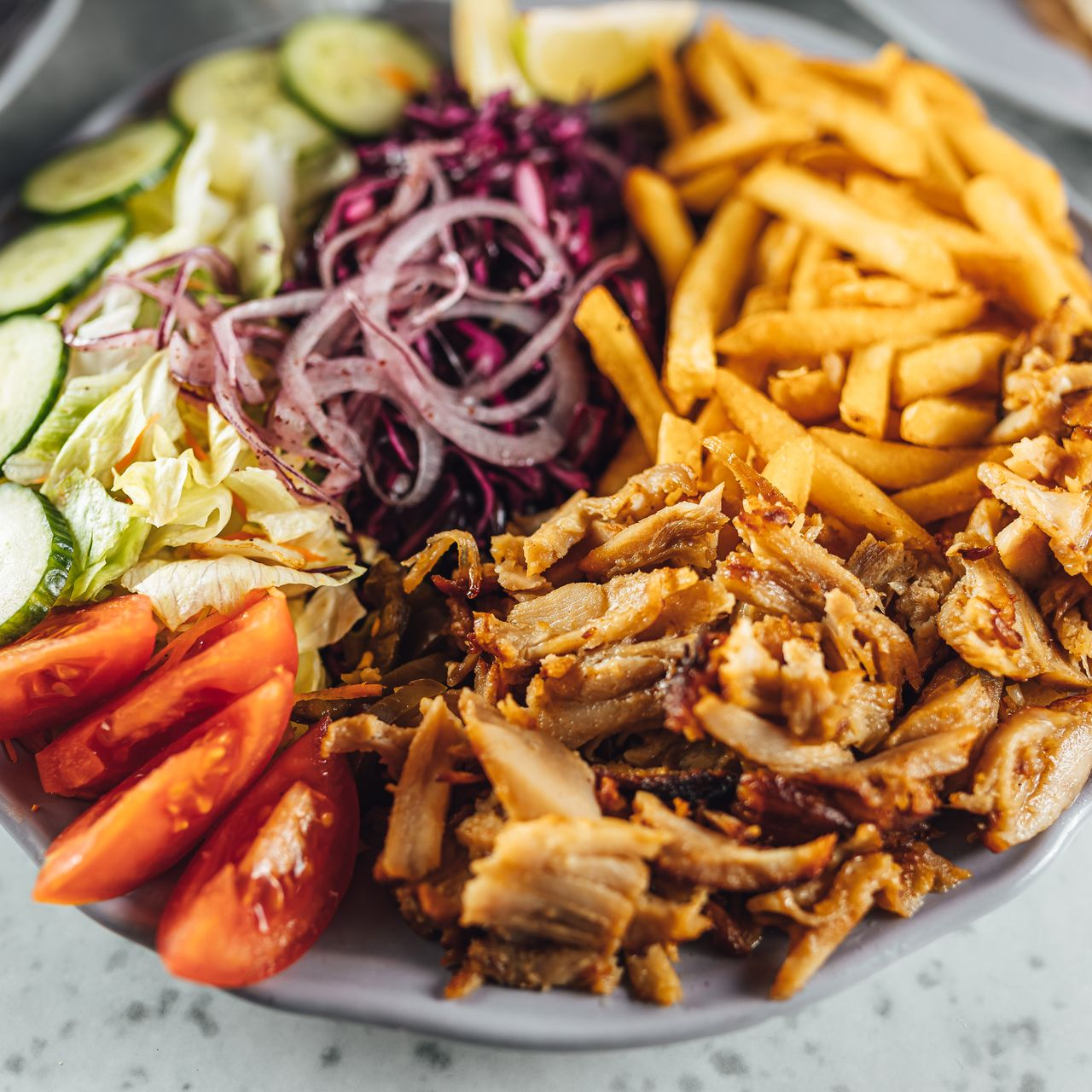 Assiette de shawarma avec légumes coupés en tranches, oignons rouges, tomates, concombres, frites et viande effilochée.