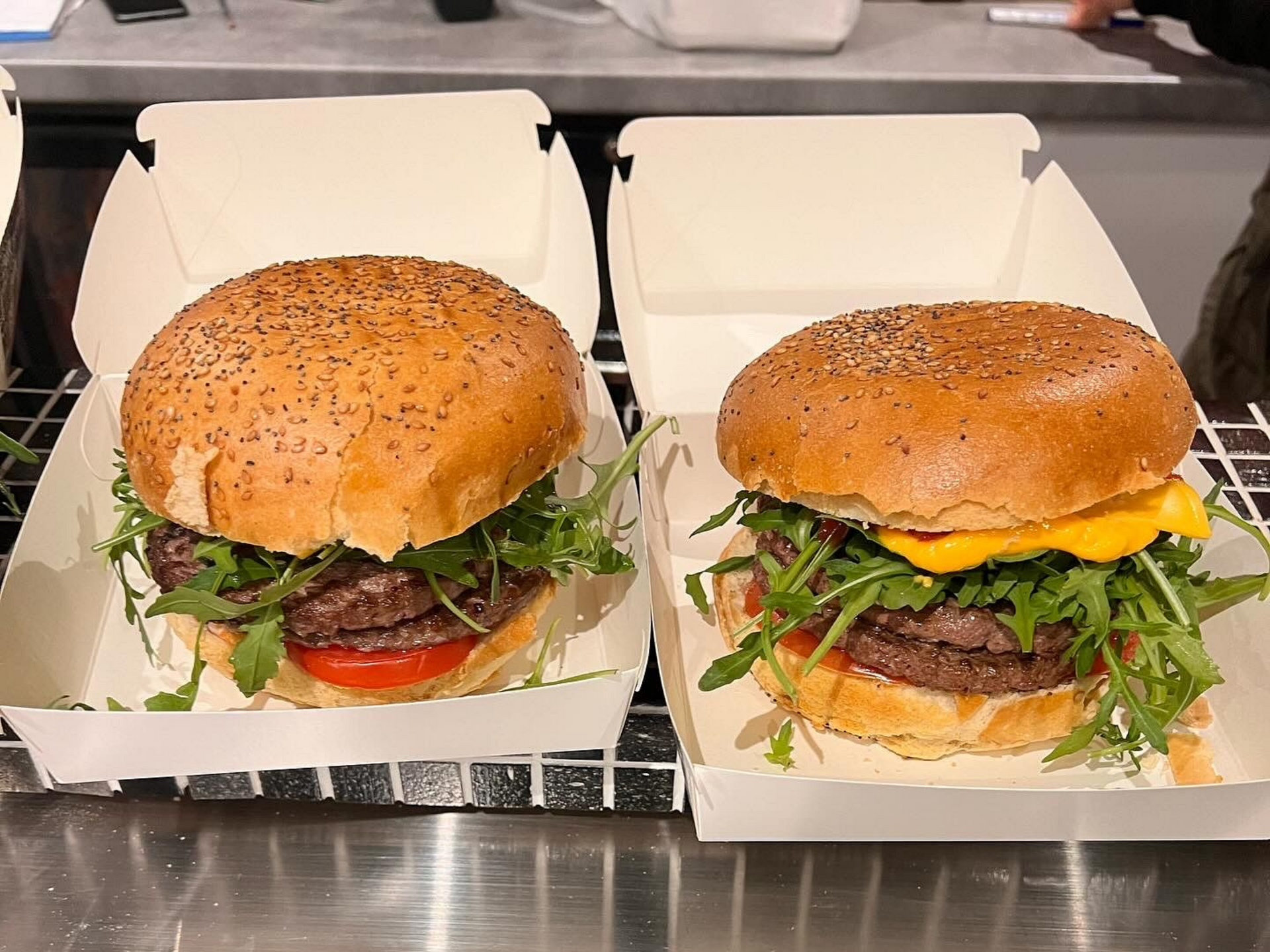 Deux cheeseburgers dans des boîtes blanches ouvertes sur un comptoir, garnis de pains au sésame et de verdure.