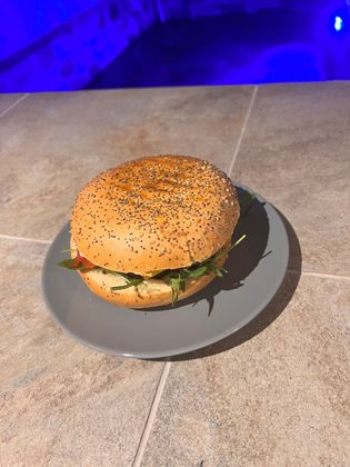 Burger aux graines de sésame sur une assiette grise posée sur une table en pierre, avec un fond éclairé en bleu.
