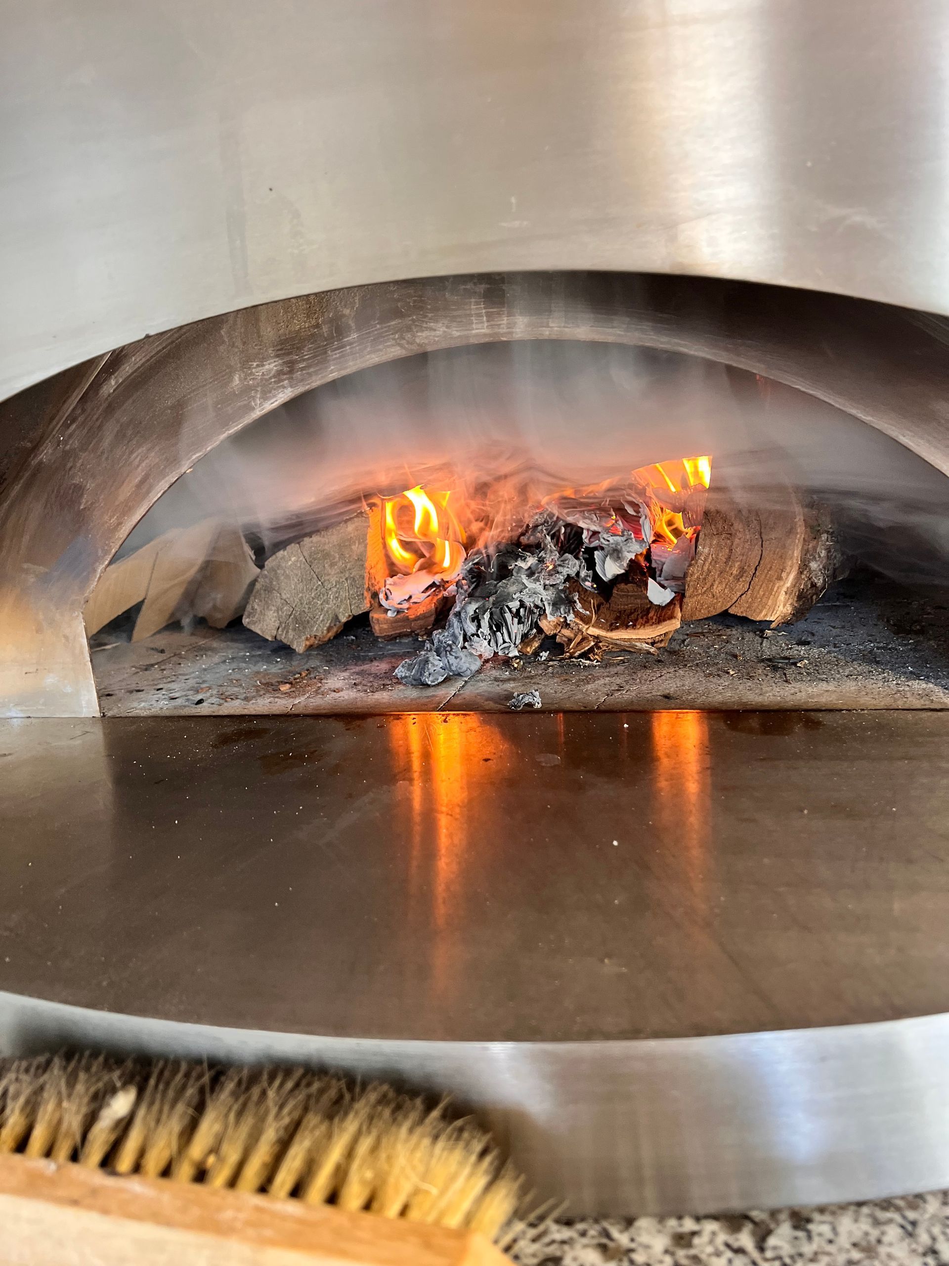 Un feu brûle dans une cheminée en acier inoxydable, avec des bûches et des braises incandescentes.