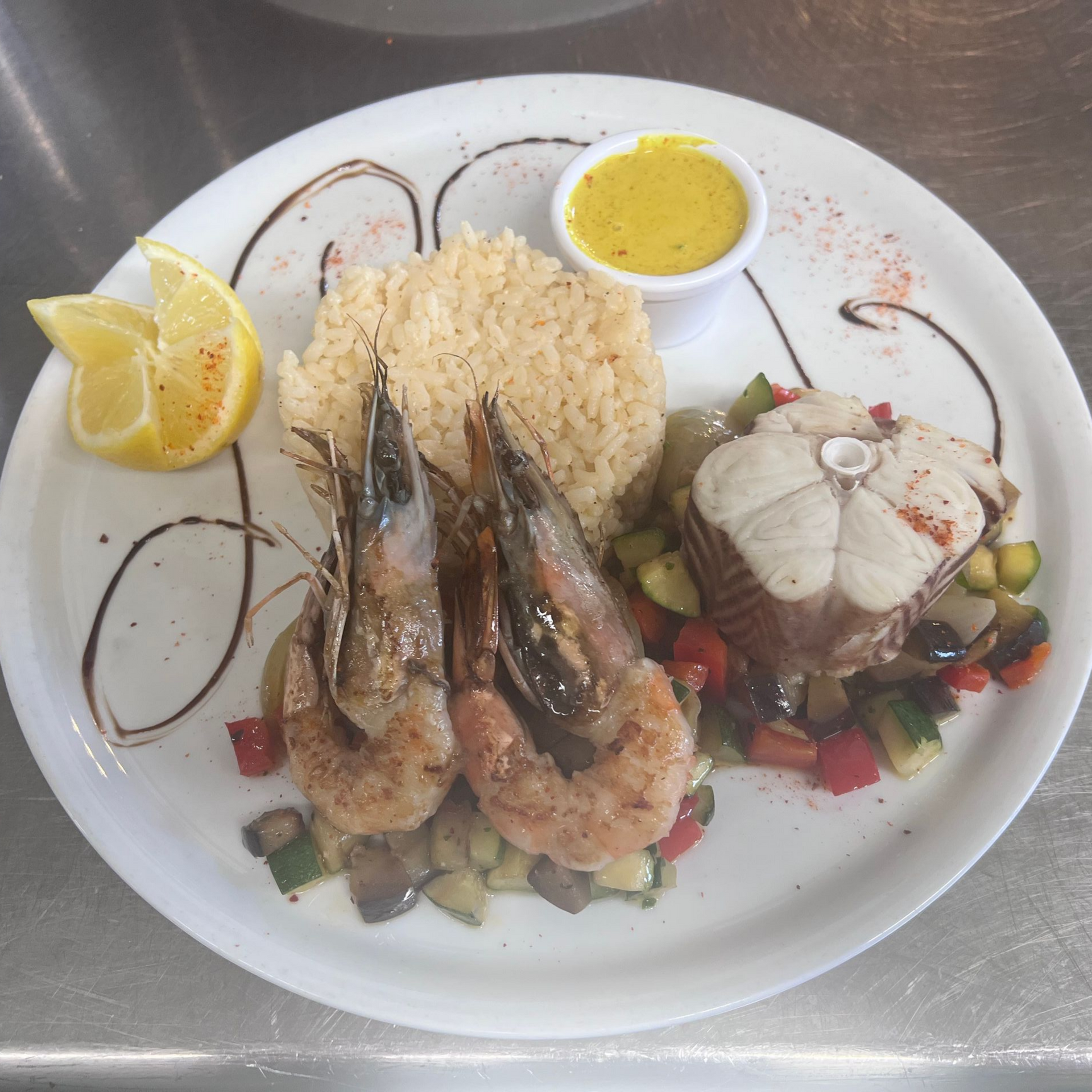 Plat de fruits de mer servi avec du riz, des quartiers de citron, de la sauce et des légumes dans une assiette blanche.