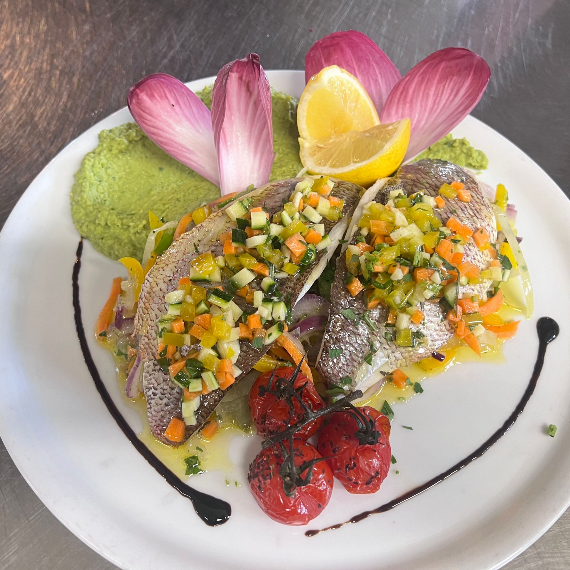 Filets de poisson garnis de légumes coupés en dés, présentés sur une assiette blanche, agrémentés de citron et de sauce.