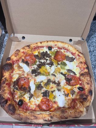 Pizza ouverte dans une boîte en carton, garnie de fromage, d'olives, de poivrons et d'herbes.