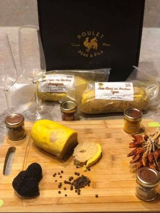 Terrines et bocaux de foie gras disposés sur une planche en bois avec du pain, des grains de poivre et des épices.