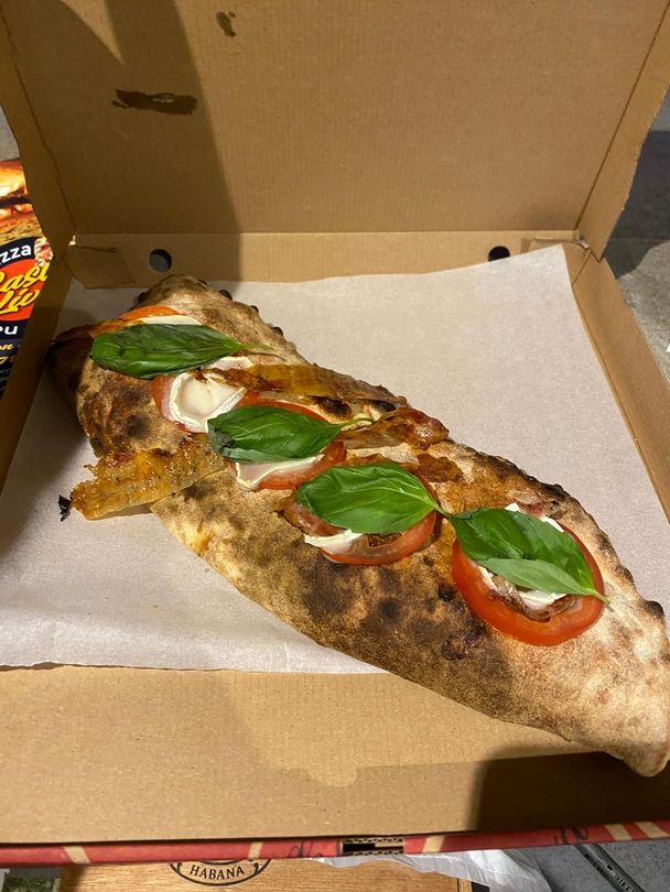 Une part de pizza avec basilic, tomate et fromage fondu dans une boîte à emporter ouverte.