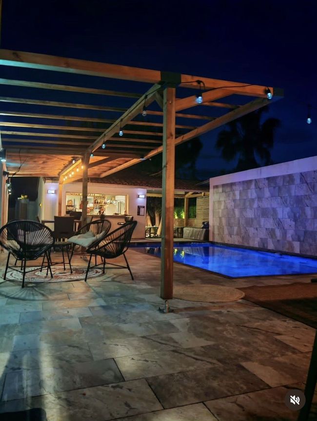 Terrasse au bord de la piscine avec un petit bar, trois tabourets et une piscine carrelée au premier plan.