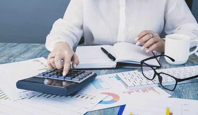 Una mujer está sentada en una mesa usando una calculadora.