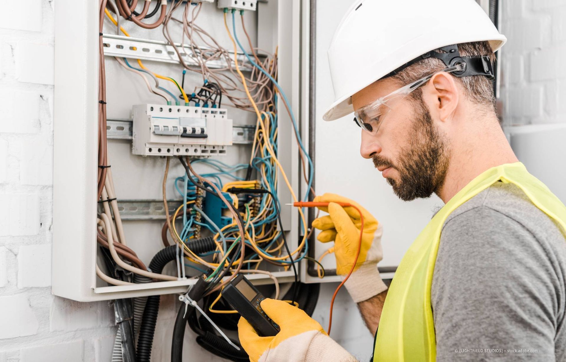 Ein Elektriker mit Schutzhelm und Handschuhen prüft die Drähte im Inneren eines Verteilerkastens.