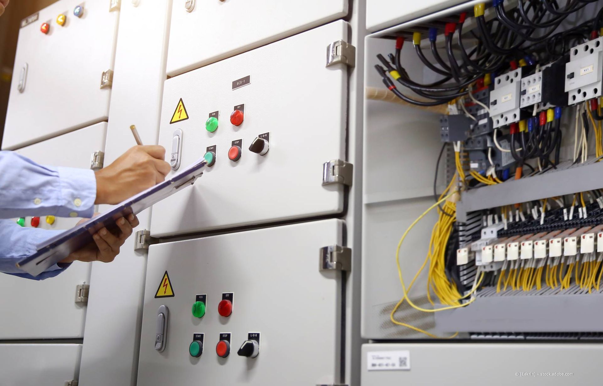 Eine Person inspiziert einen elektrischen Schaltschrank und schreibt dabei auf ein Klemmbrett.