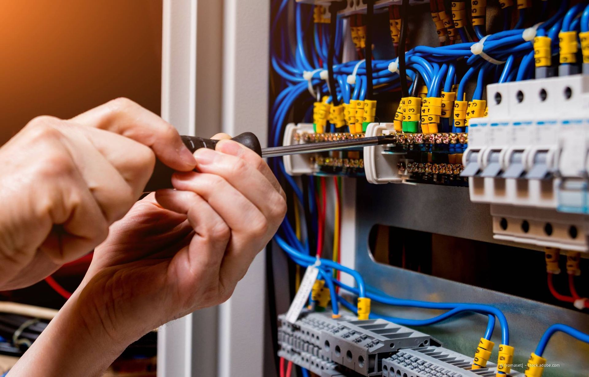 Hände benutzen einen Schraubendreher, um an einer Schalttafel mit elektrischen Leitungen und Schaltkreisen zu arbeiten.