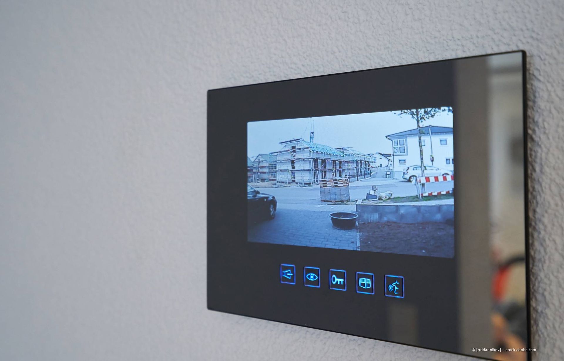 Schwarzes Display einer Video-Türklingel an einer grauen Wand, das eine Straßenansicht zeigt.