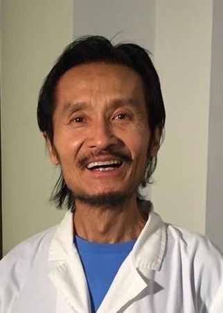 Ein Mann mit Bart trägt einen weissen Kittel und lächelt.