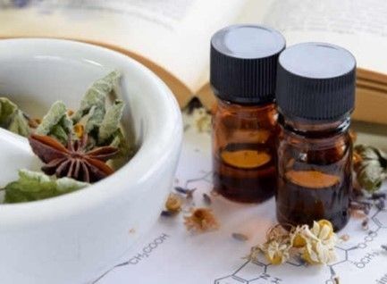 Un mortaio e un pestello con erbe essiccate e due bottiglie di olio essenziale.