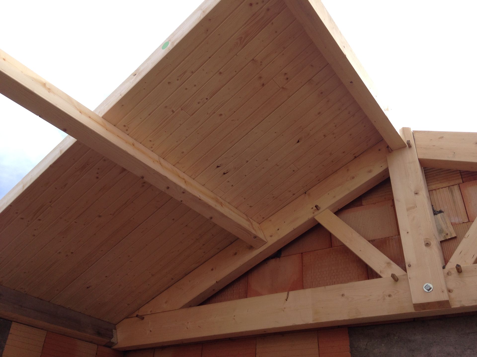 Charpente de toit en bois avec planches, soutenue par un mur de briques.