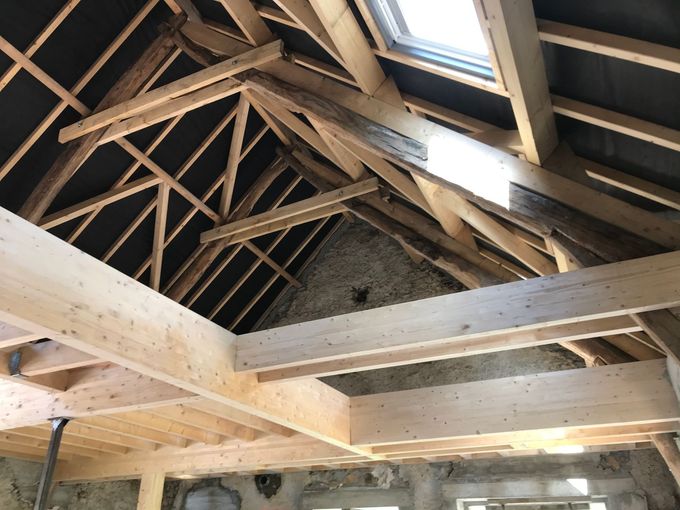 Charpente en bois (poutres et chevrons) dans un grenier, avec un puits de lumière, illustrant la construction.