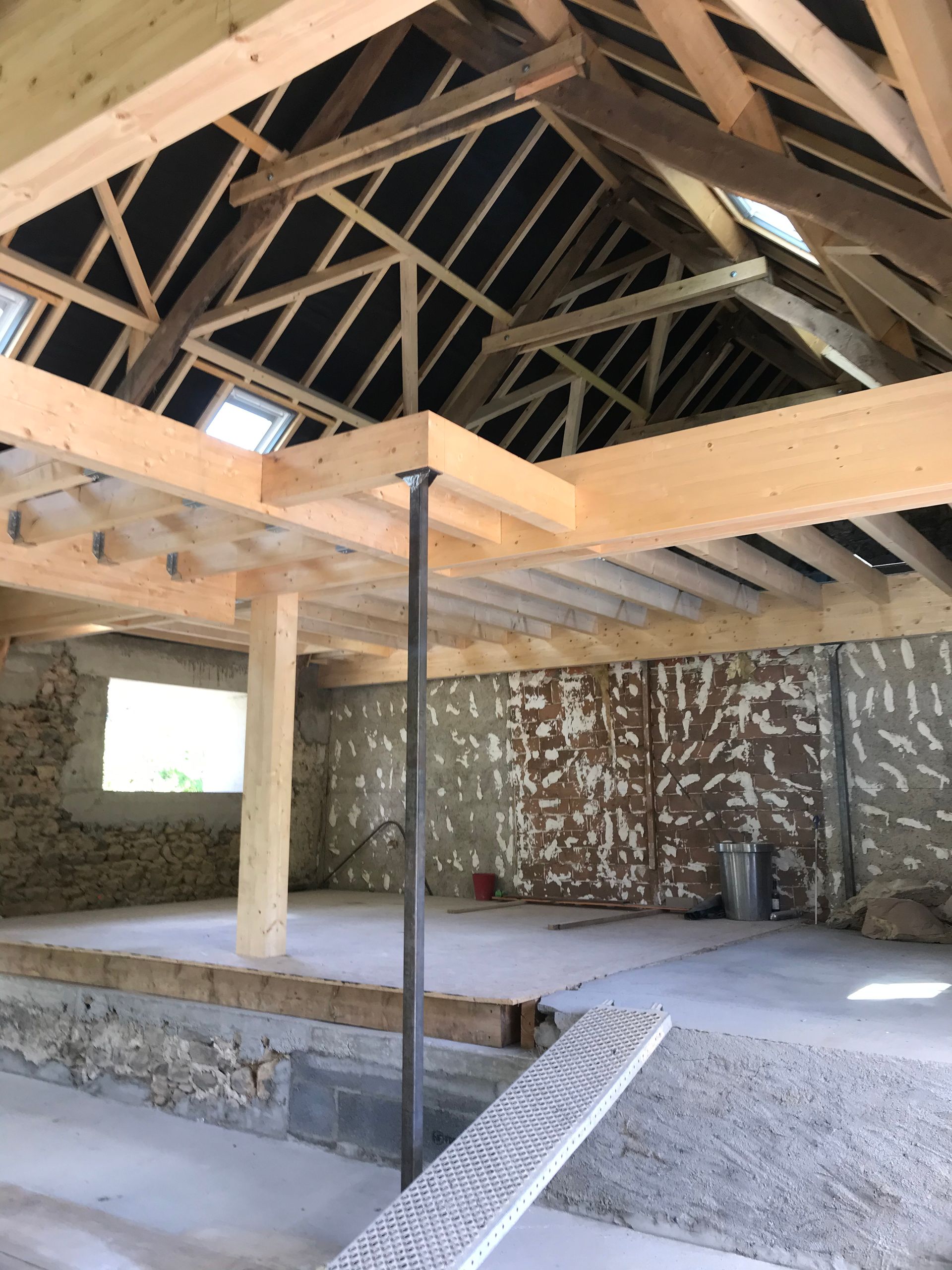 Intérieur d'un bâtiment en construction, montrant des poutres en bois, un sol et des murs apparents.