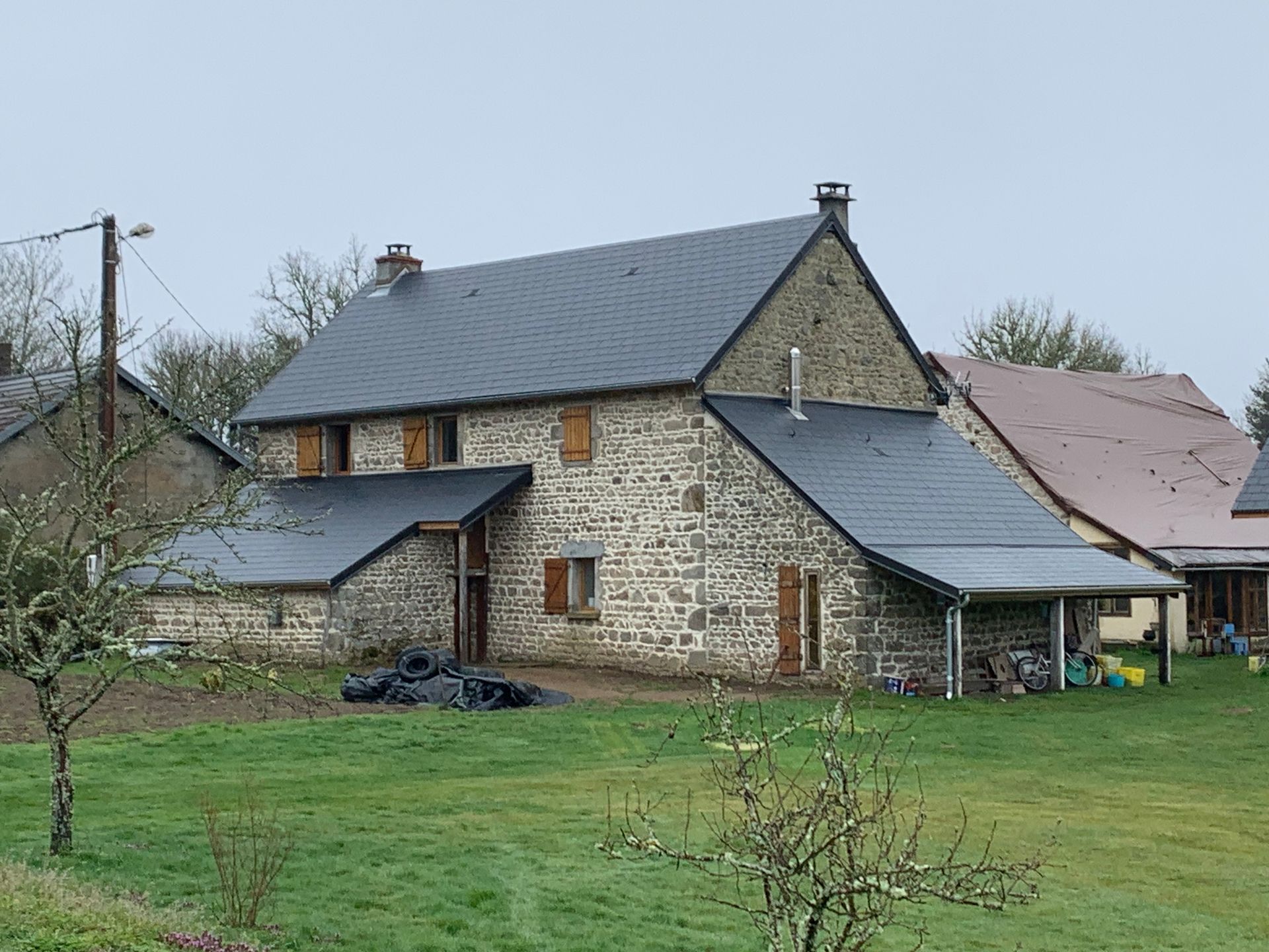 Maison en pierre au toit d'ardoises, sur un terrain herbeux sous un ciel couvert.