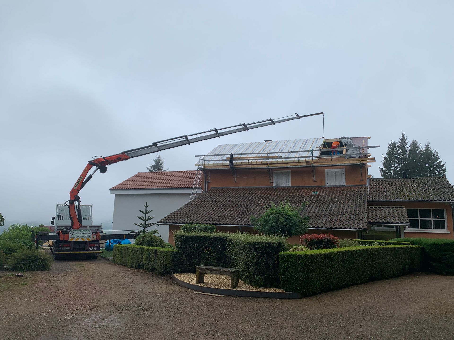 Grue participant à la construction du toit d'une maison, par temps couvert.