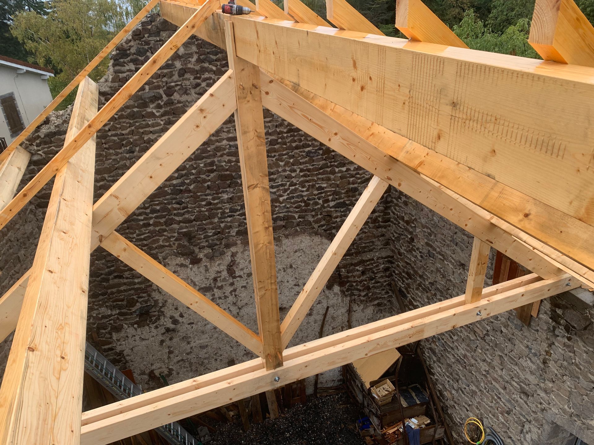Charpente de toit en bois en construction, adossée à un mur de pierre.