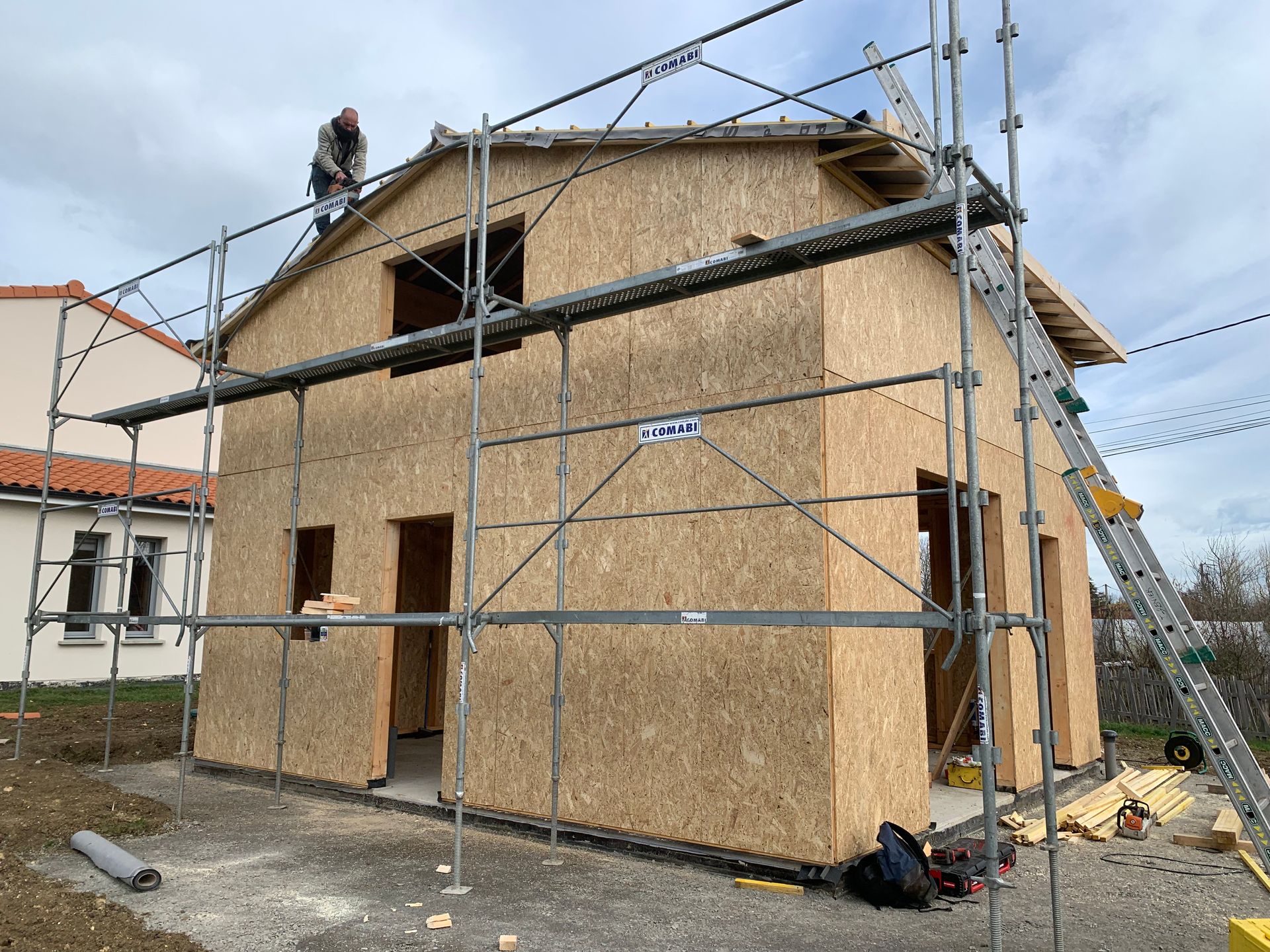 Bâtiment de deux étages en construction avec des échafaudages. Un ouvrier sur le toit.