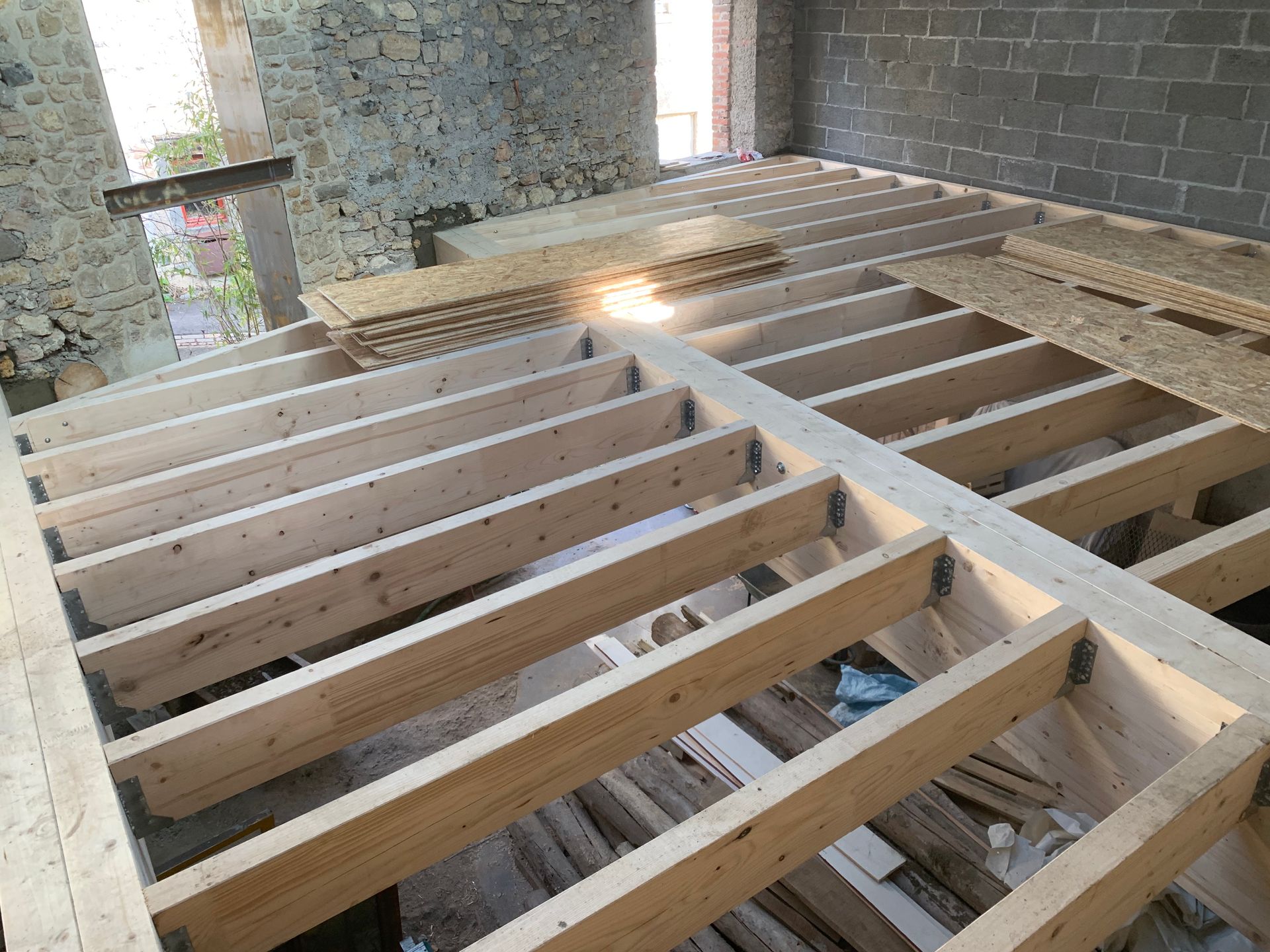 Installation de solives en bois dans une pièce aux murs de pierre et de brique.