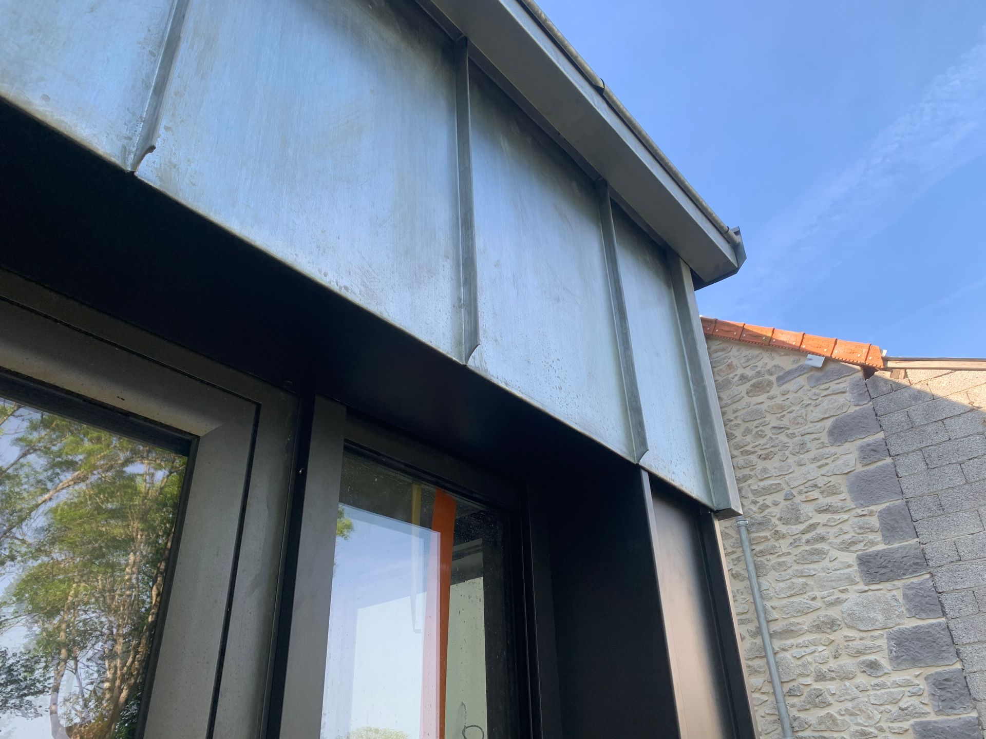 Vue extérieure d'un bâtiment à façade métallique et fenêtre, sur fond de ciel bleu.