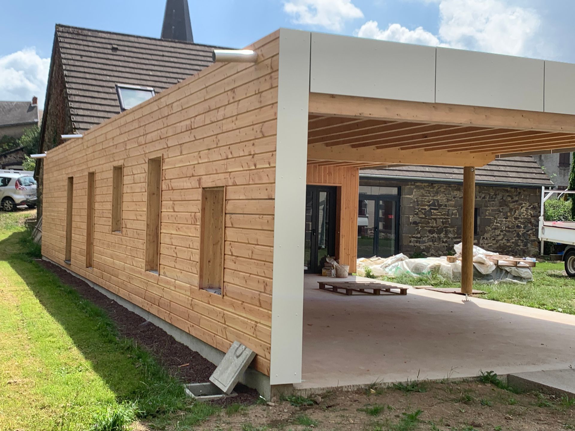 Bâtiment en bois avec abri de voiture, fenêtres et finitions de toit blanches.