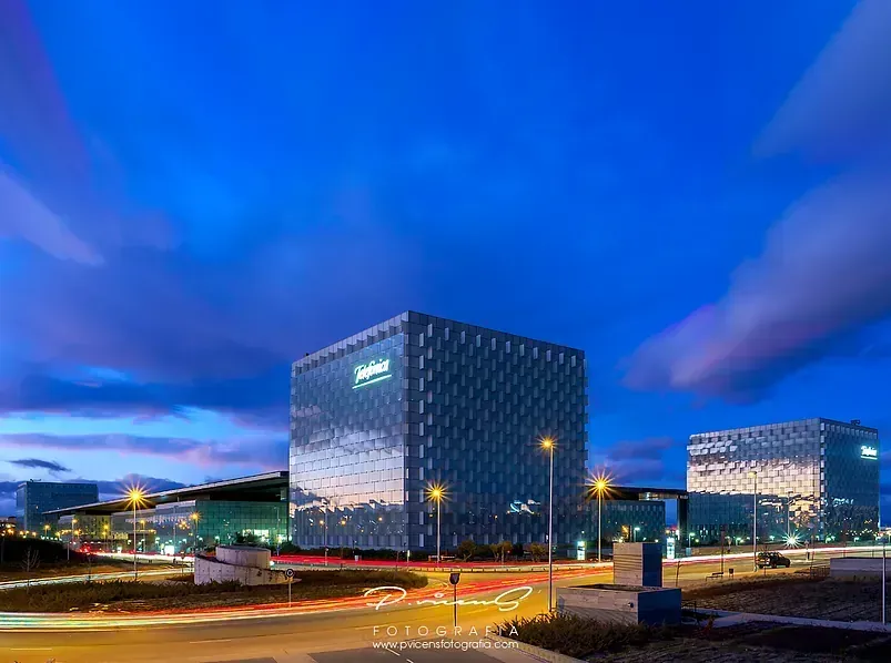 Un grupo de edificios están iluminados por la noche con un cielo azul de fondo.