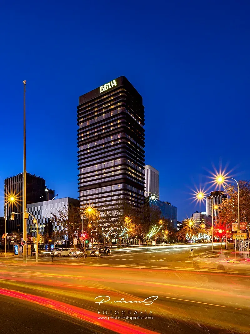 Una fotografía de larga exposición de una calle de la ciudad por la noche con un edificio alto al fondo.