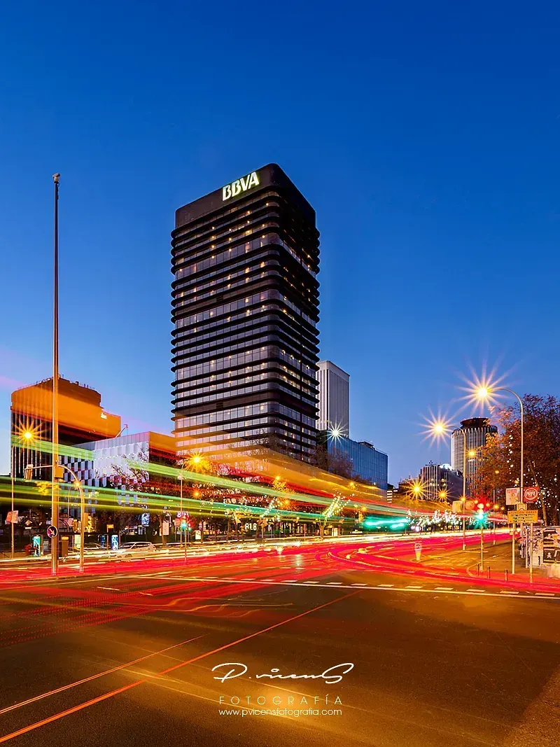 Una fotografía de larga exposición de una calle de la ciudad por la noche con un edificio alto al fondo.