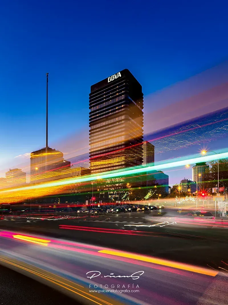 Una fotografía de larga exposición de una ciudad de noche con un edificio al fondo.