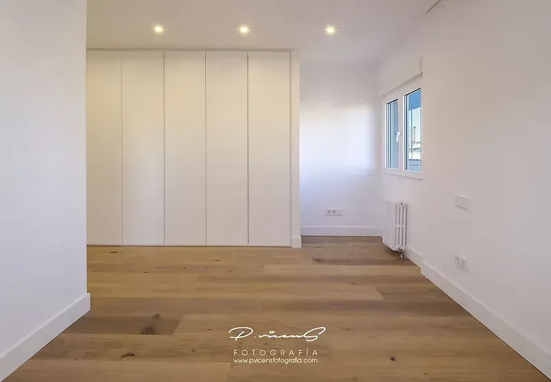Una habitación vacía con pisos de madera y paredes blancas.