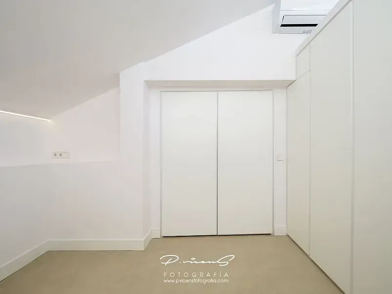Una habitación con techo inclinado y armarios blancos.