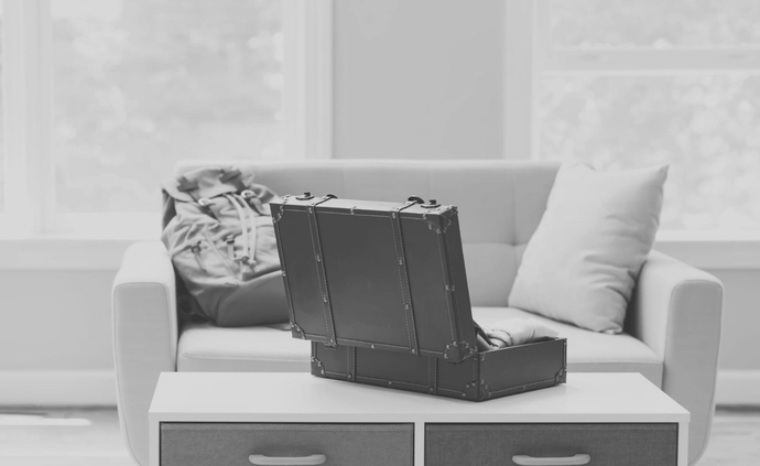 Una maleta vintage abierta de color marrón oscuro reposa sobre una mesa de centro frente a un sofá gris claro