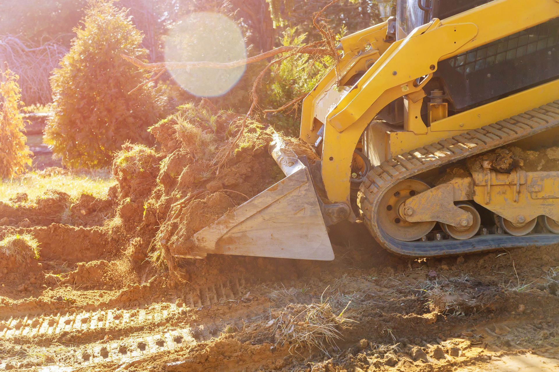 Un engin de chantier jaune déplace de la terre et des broussailles sur un chantier ensoleillé