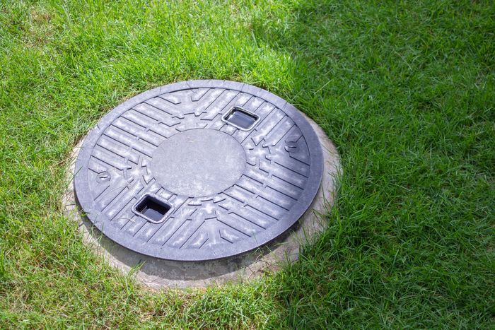 Plaque d'égout ronde en métal, entourée d'herbe verte, avec deux ouvertures rectangulaires