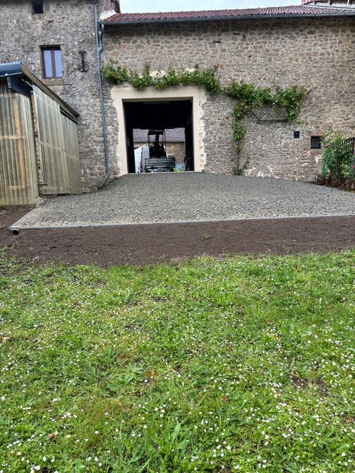 Bâtiment en pierre avec une petite porte et une rampe en gravier à côté d'une cour gazonnée