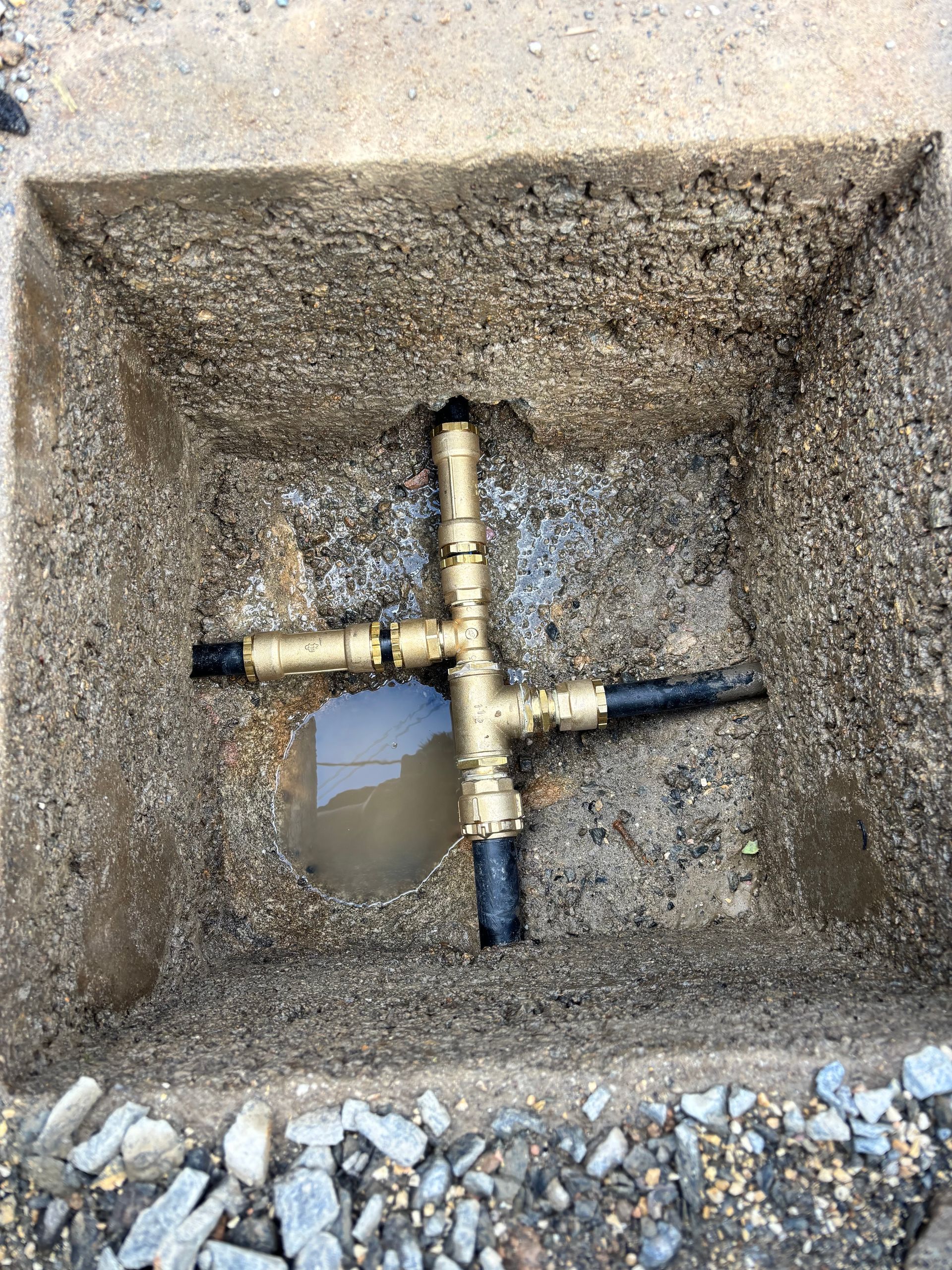 Coffre-fort en béton avec raccords et tuyaux de plomberie en laiton à l'intérieur, entouré de gravier.