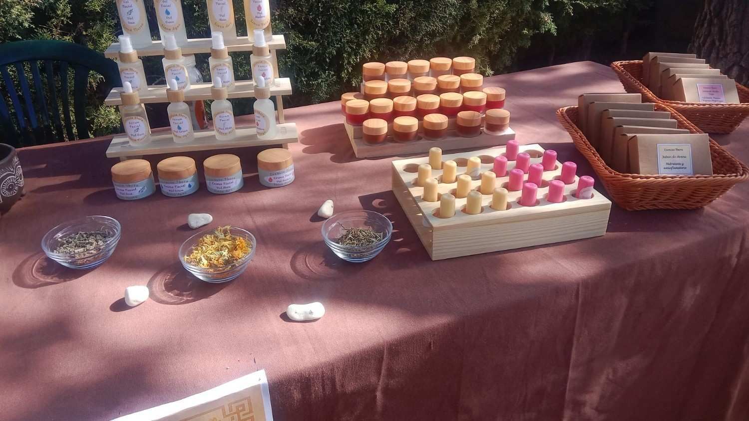 En una mesa al aire libre se exhiben productos naturales para el cuidado de la piel, como aceites embotellados.