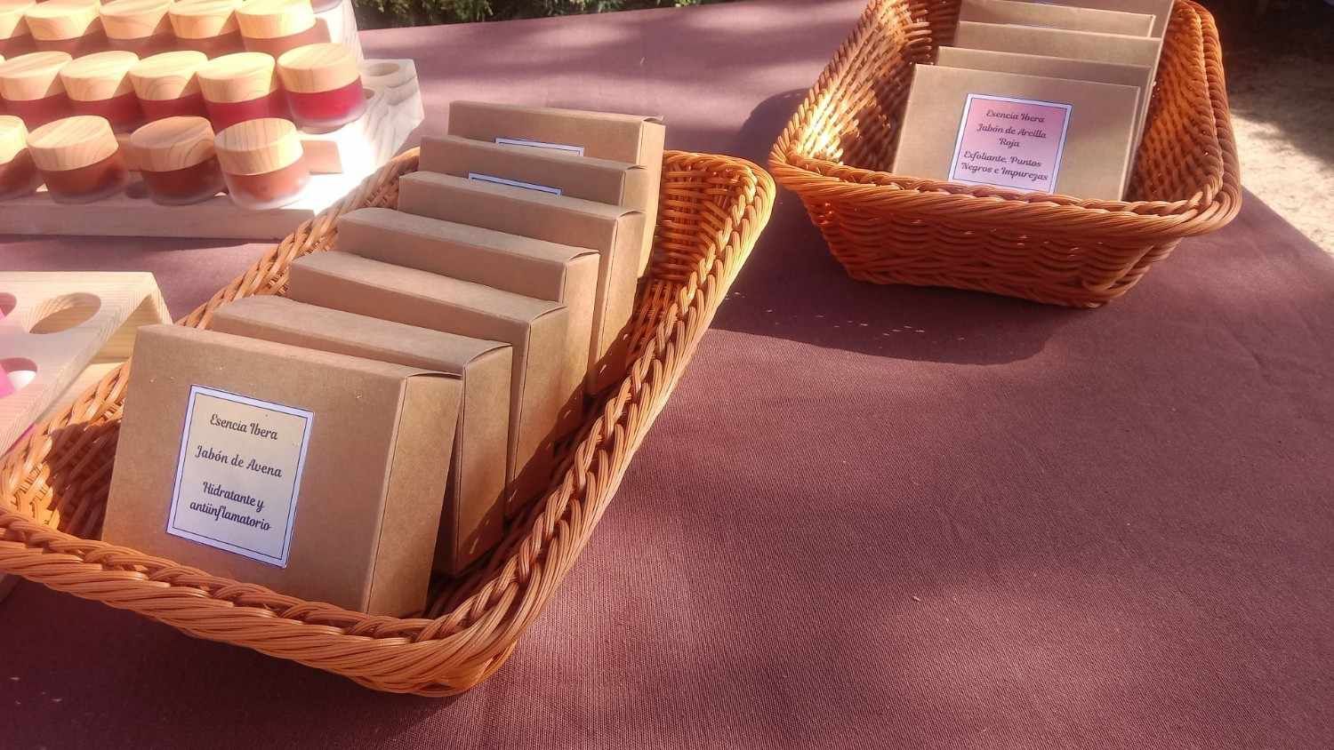 Dos cestas tejidas sobre una mesa, llenas de pequeños artículos artesanales empaquetados, y una vitrina con pequeños frascos.