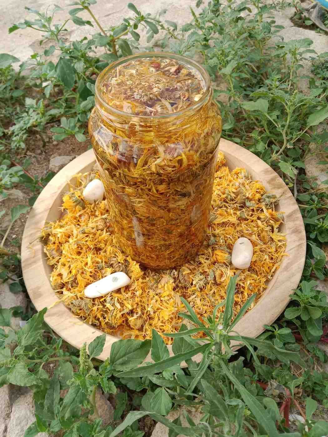 Un frasco de vidrio lleno de flores de caléndula amarillas maceradas en aceite reposa sobre una bandeja de madera.