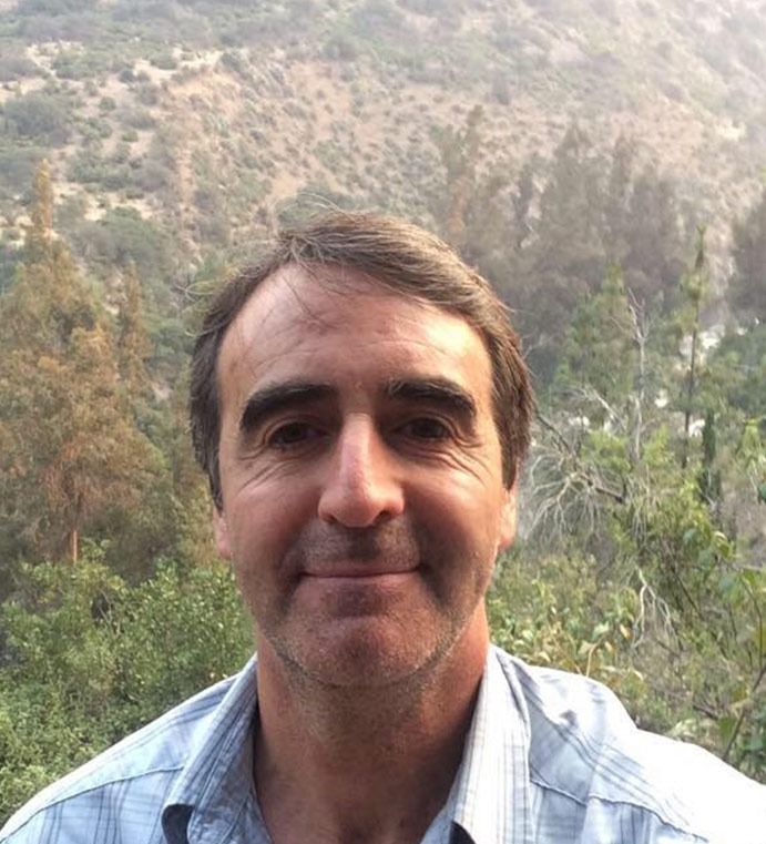 Un hombre con barba sonríe frente a una montaña.