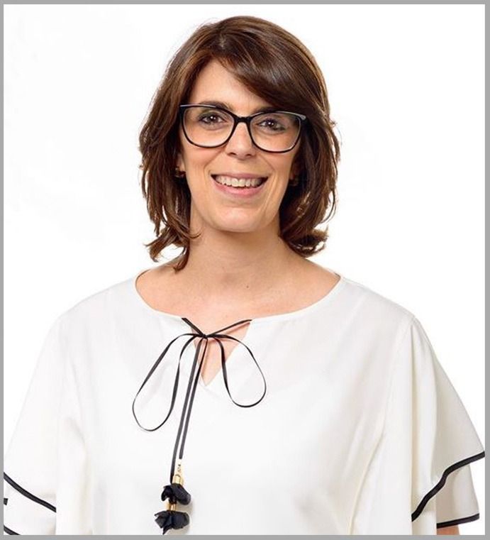 Una mujer que lleva gafas y una camisa blanca está sonriendo.
