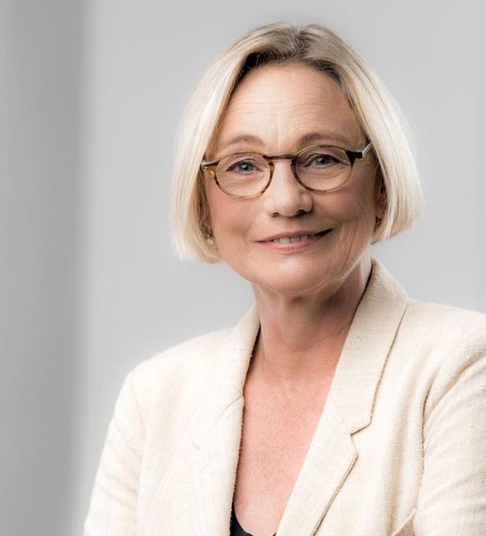 Una mujer que lleva gafas y una chaqueta blanca sonríe para la cámara.