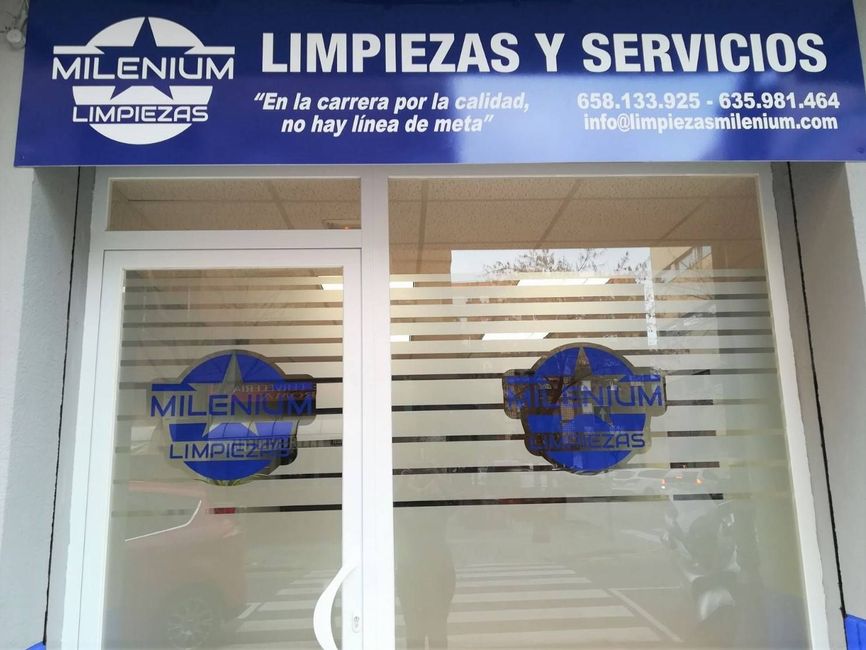 Un par de guantes de goma rosas y una botella de líquido limpiador sobre una superficie blanca.