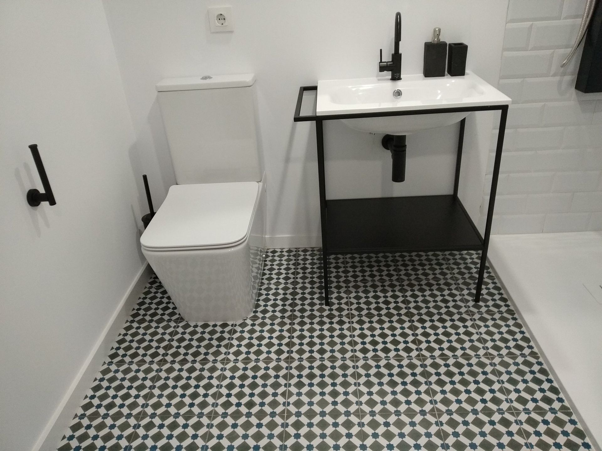 Baño con inodoro blanco, lavabo negro y suelo estampado.